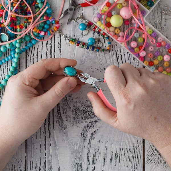 Handen maken sieraden met kralen en turquoise steen op houten tafel vol kleurrijke kralen en gereedschap.