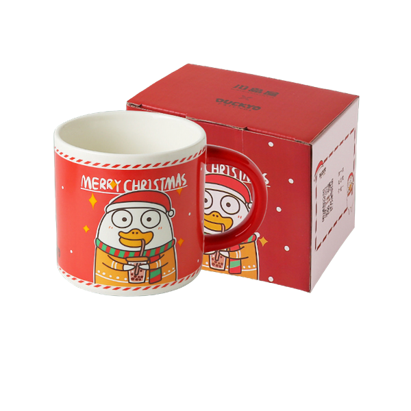 Rode kerstbeker met cartoonfiguur van een eend en tekst Merry Christmas, staan naast bijpassende verpakking.