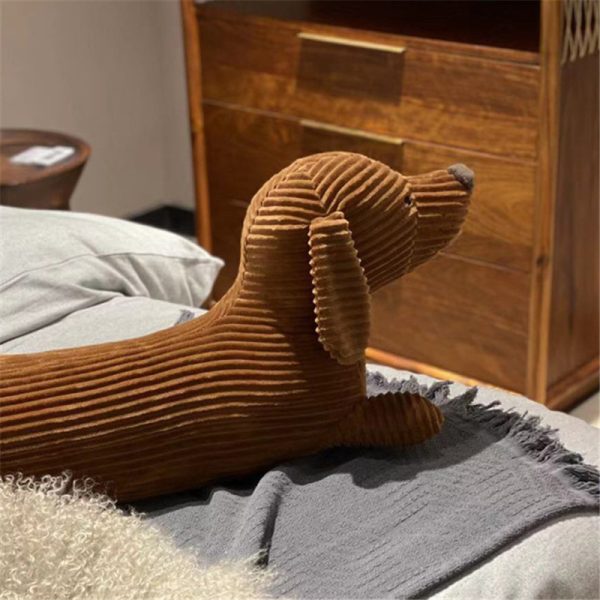 Pluche hond knuffel op bed met grijze deken en houten kast op achtergrond. Sfeervol slaapkamerdecor.