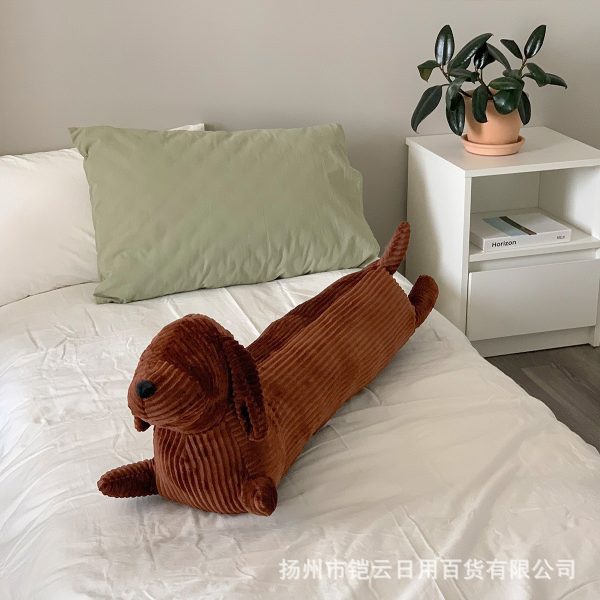 Pluche hondenkussen op een bed naast een groene plant en boeken, zorgt voor een knusse slaapkamerinrichting.
