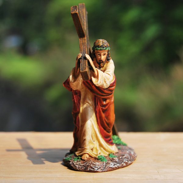 Beeldje van man met kruis, symbolisch voor religie en offer, tegen groene achtergrond op houten oppervlak.