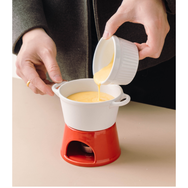 Hand giet gesmolten kaas in een fonduepan op rood fornuisje voor een gezellige maaltijd thuis.