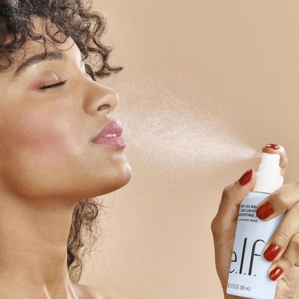 Vrouw gebruikt make-up fixingspray op gezicht met gesloten ogen voor langdurige make-up, bruine achtergrond, e.l.f. verpakking.