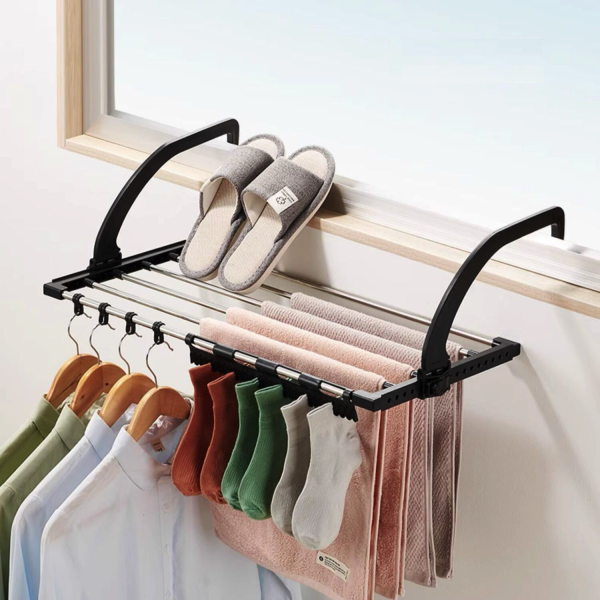 Opvouwbaar droogrek met kleding, handdoeken en slippers, bevestigd aan het raam voor ruimtebesparend drogen.