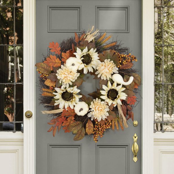 Herfstkrans met pompoenen en zonnebloemen siert een grijze deur, omgeven door herfstbladeren en bessen.