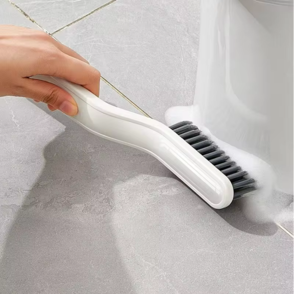 Hand gebruikt witte borstel om vloer en rand van toilet schoon te maken. Hygiënisch reinigen van badkameroppervlakken.