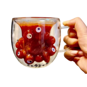 Transparante mok met rode vloeistof en drijvende octopus met ogen, vastgehouden door een hand.